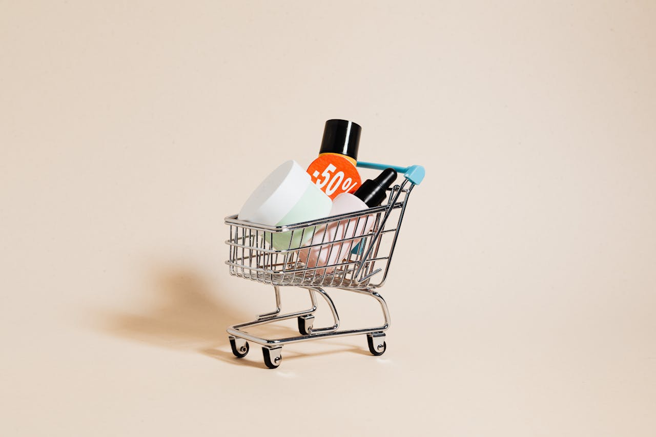 Mini shopping cart with cosmetics and a 50% discount sign on a neutral background.